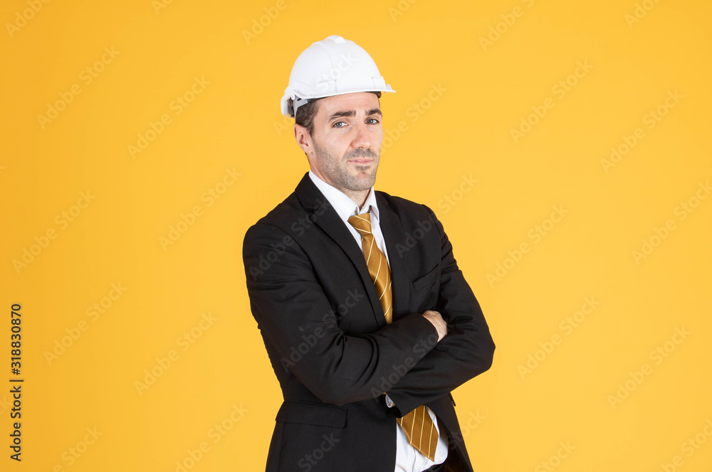 Young handsome businessman wears suit and construction helmet on isolated yellow background.