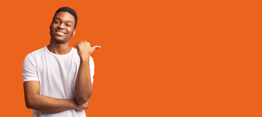 Young afro guy pointing at copy space with thumb up
