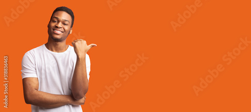 Young afro guy pointing at copy space with thumb up