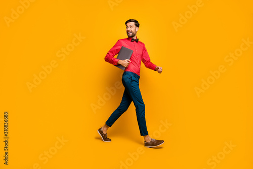Full length profile photo of amazing business man walking corporate meeting training carry laptop wear stylish red shirt bow tie blue pants shoes isolated yellow color background