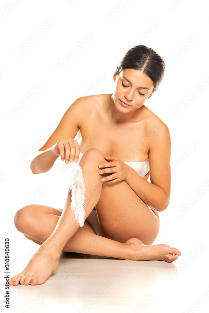 Obraz premium Beautiful young woman touches her smooth legs with white feather