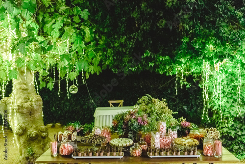 Table with sweet desserts in a garden at night, illuminated by LED lights.
