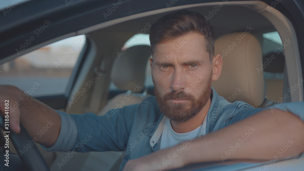 Amazing portrait of young cheerful man smiling at lovely sunset sitting in modern luxurious car staying in city center. Amazing portrait of young cheerful man smiling at lovely sunset sitting in modern luxurious car staying in city center.