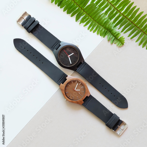 Top view of 2 black wooden watches with green leaf
