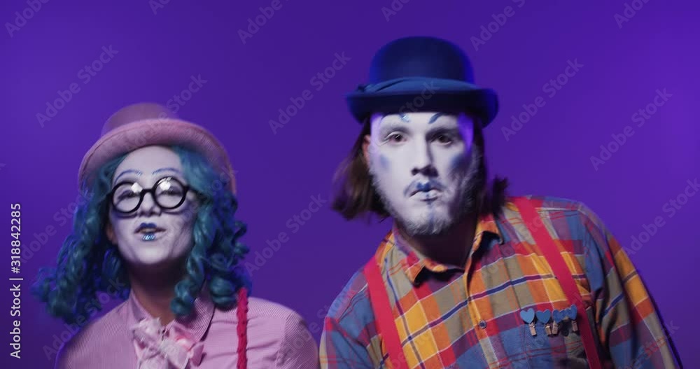 A beautiful colorful pair of funny clown mimes performing emotional synchronously dance on isolated purple background. Positive success A beautiful colorful pair of funny clown mimes performing emotional synchronously dance on isolated purple background. Positive success