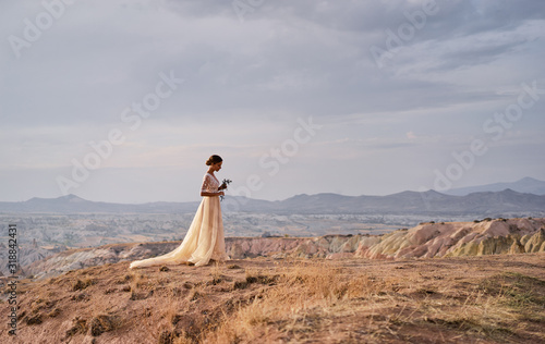 Fotografija Young bride standing on top of a ridge waiting for her groom.