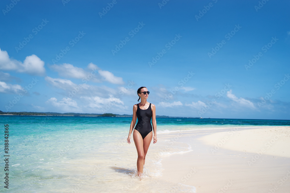 Vacation on the seashore. Back view of young woman walking on the beautiful tropical white sand beach.