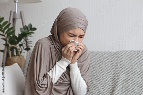 Sick muslim woman blowing runny nose to napkin at home photo