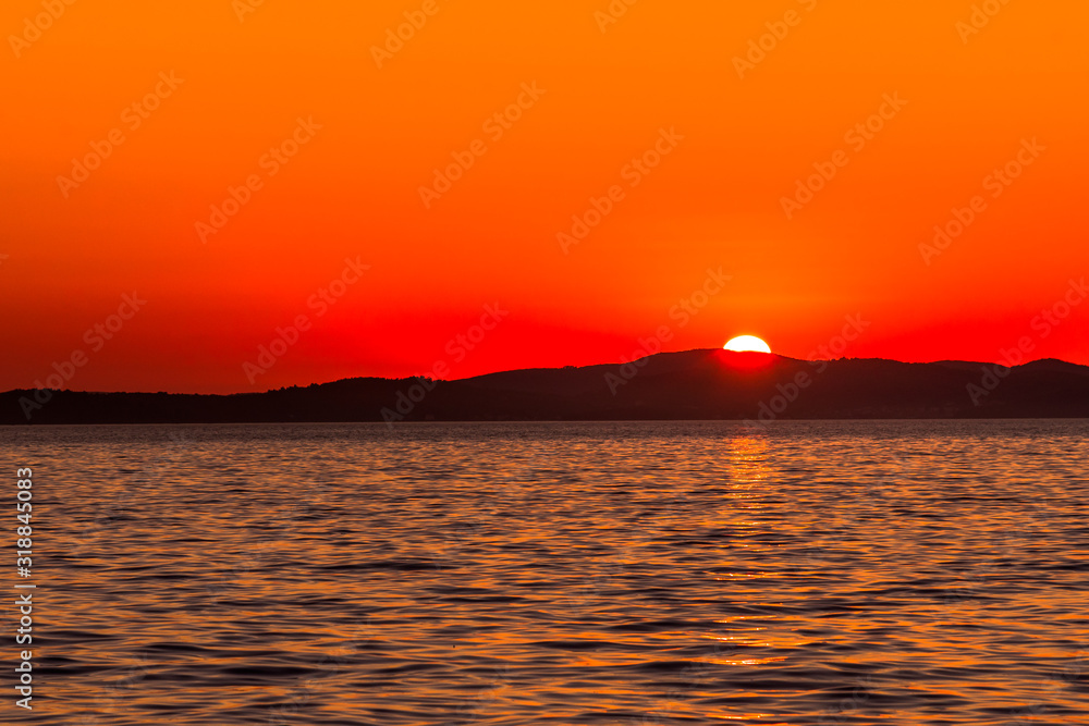 Beautiful orange sunset over the sea with sun on the mountains horizon, view from beach in Zadar, Dalmatia, Croatia, Europe Beautiful orange sunset over the sea with sun on the mountains horizon, view from beach in Zadar, Dalmatia, Croatia, Europe
