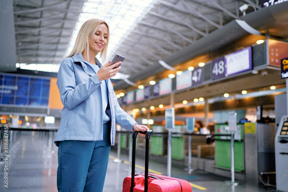 Travel and technology. Online check-in. Female traveler using smartphone waiting for boarding near registration desk line. - obrazy, fototapety, plakaty 