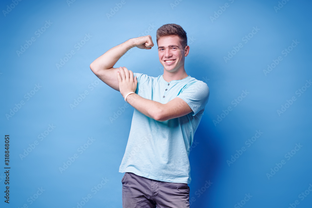Strong and energy. Handsome young man showing bicep on his arm. Studio portrait with blue background. Strong and energy. Handsome young man showing bicep on his arm. Studio portrait with blue background.