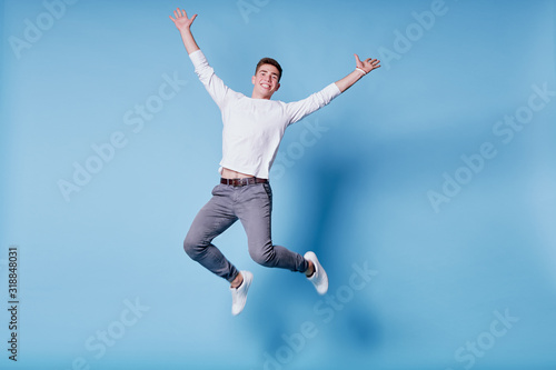 Colorful studio portrait of happy young man jumping against blue background. photo