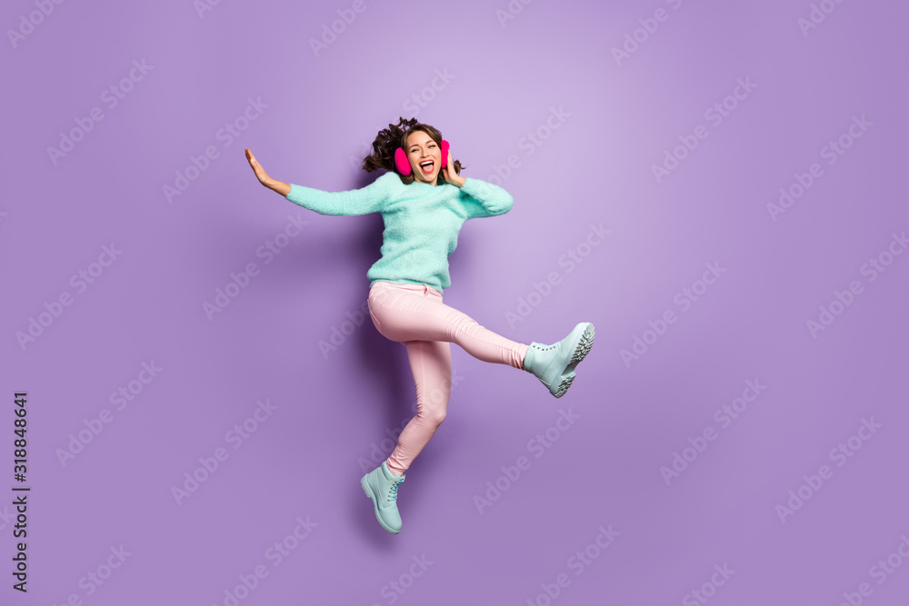 Full body photo of pretty lady jumping high up excited good mood rejoicing dancing wear fuzzy pullover pink ear covers pastel pants boots isolated purple color background
