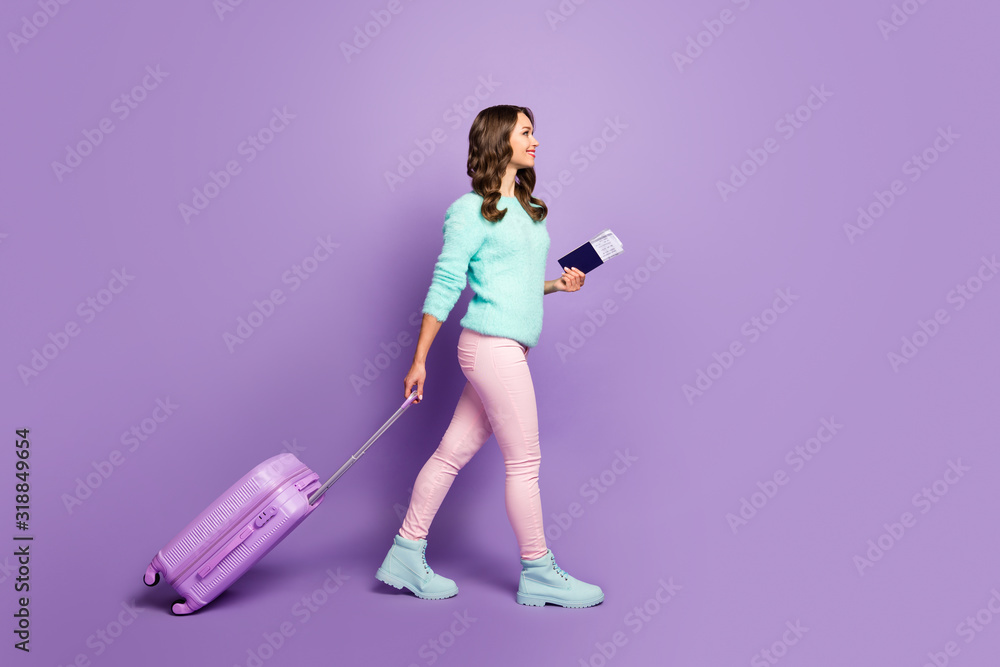Full length photo of pretty funny lady walking airport registration with tickets rolling trip suitcase wear fuzzy sweater pink pastel trousers boots isolated purple color background Full length photo of pretty funny lady walking airport registration with tickets rolling trip suitcase wear fuzzy sweater pink pastel trousers boots isolated purple color background