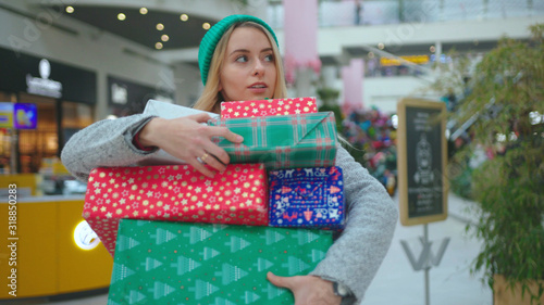 Close up face beautiful woman wear hat walking with Christmas presents try holds the boxes carefully in shopping mall smile happy buy new year holiday portrait slow motion