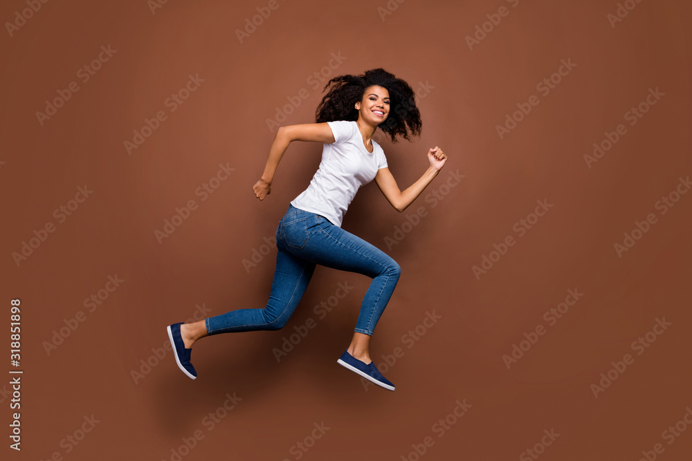 Full length profile photo of funny dark skin lady jumping high sports competitions participant rushing finish line wear white t-shirt jeans isolated brown color background Full length profile photo of funny dark skin lady jumping high sports competitions participant rushing finish line wear white t-shirt jeans isolated brown color background
