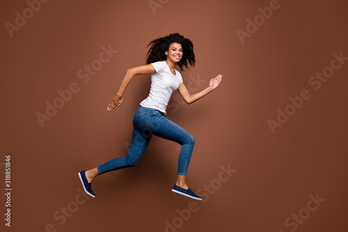 Fototapeta Naklejka Na Ścianę i Meble -  Full size profile photo of amazing dark skin lady jumping high sports competitions rushing finish line winner mood wear casual white t-shirt jeans isolated brown color background