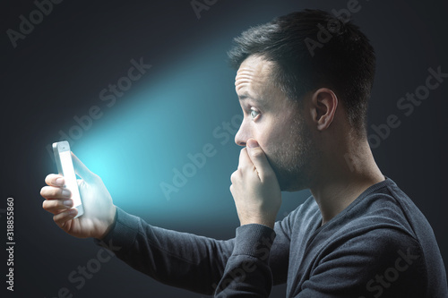 Foto Appalled man looking at his glowing smartphone screen