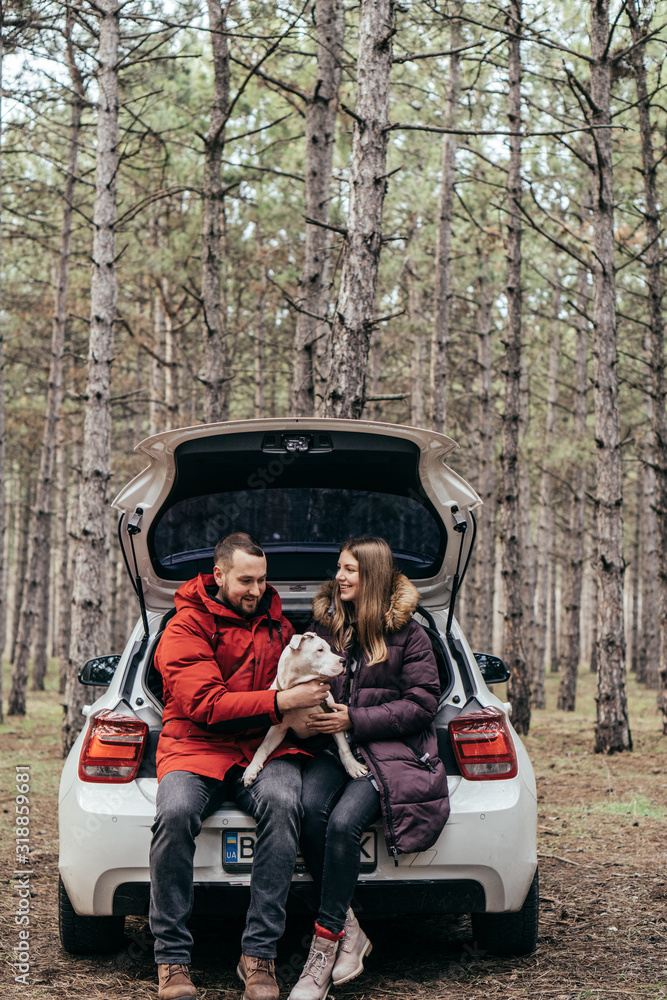 Young happy family with dog sitting in the car in the autumn forest. Active lifestyle. Happy look. Holiday in forest Young happy family with dog sitting in the car in the autumn forest. Active lifestyle. Happy look. Holiday in forest