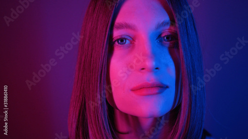 Close-up shot of splendid young woman with blue eyes. Wonderful girl turning around, looking at camera. Beautiful features. Neon lighting. Bob hairstyle. Stylish, lit