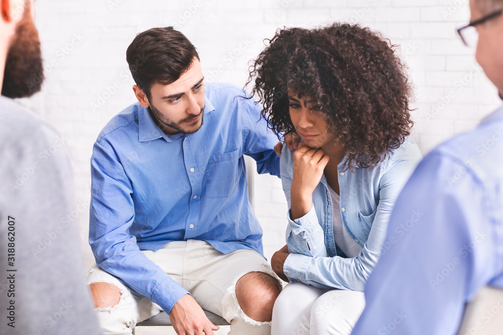 Fototapeta premium Supportive people comforting depressed black woman at group therapy meeting