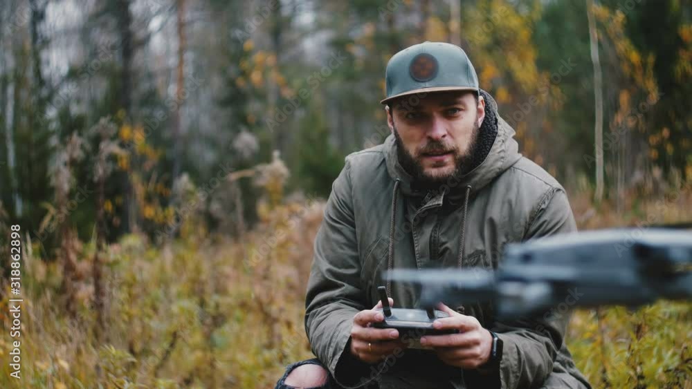 Young happy casual bearded Caucasian videographer man is controlling drone camera aircraft with remote in autumn forest. Young happy casual bearded Caucasian videographer man is controlling drone camera aircraft with remote in autumn forest.