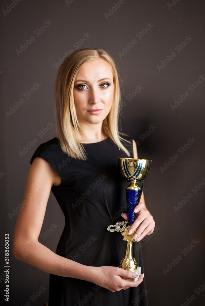 Beautiful young successful blonde woman with gold Cup winner on dark background Beautiful young successful blonde woman with gold Cup winner on dark background