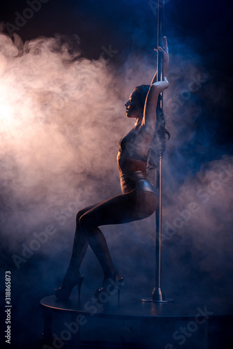 side view of attractive stripper in fishnet tights dancing striptease near pylon on blue with smoke photo