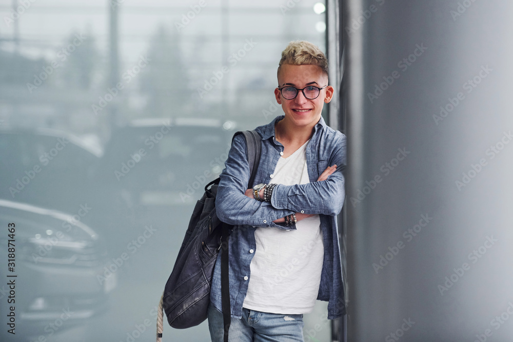 Young hipster guy in nice clothes stands indoors against grey background