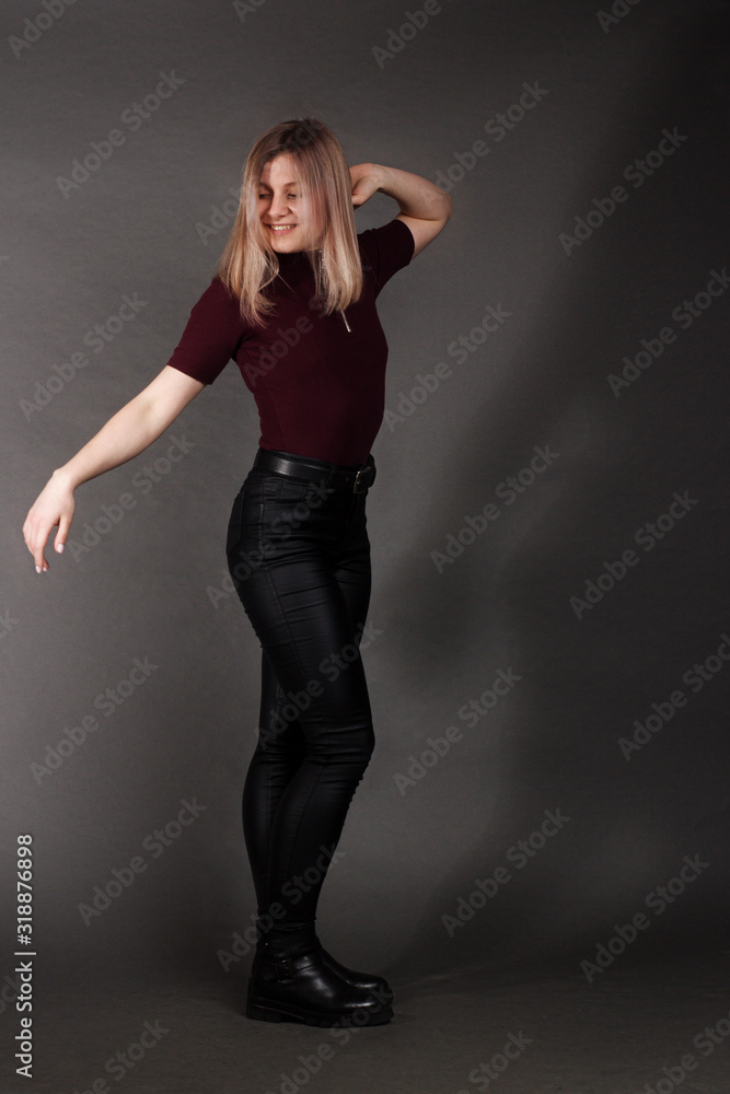growth Portrait of the blonde in the red sweater with short sleeves, leather trousers and boots. Studio shot on dark gray background growth Portrait of the blonde in the red sweater with short sleeves, leather trousers and boots. Studio shot on dark gray background