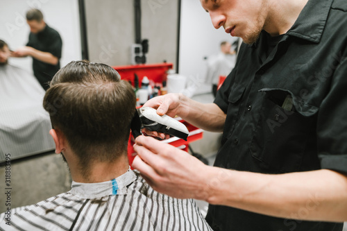 Closeup photo of a hairdresser cutting her hair with a hair clipper and comb. Professional barber creates a hairstyle for a client in a cozy men's hairdresser. Haircare in barbershop concept