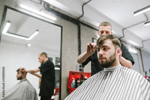 Portrait of man sitting in barbershop in chair and cutting hair in barber. Male hairdresser cuts bearded client in modern light hairdresser. Creating a Men's Hairstyle.