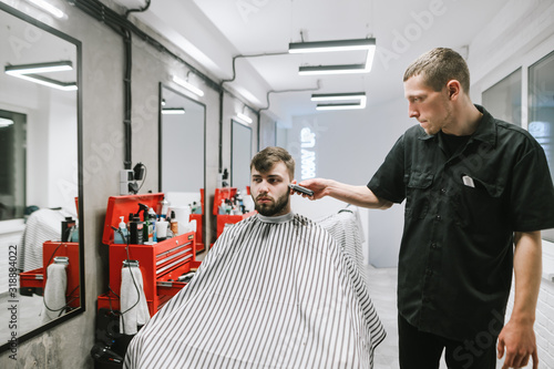 Man doing haircut in barber shop in modern light men's hairdresser.Barber clipping client in chair. Client and the male hairdresser make a haircut in a barbershop.