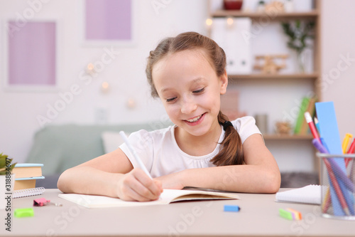 Cute little girl is doing homework in the interior of the room.