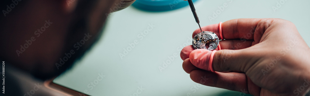Panoramic shot of watchmaker in latex fingertips setting wristwatch detail with screwdriver Panoramic shot of watchmaker in latex fingertips setting wristwatch detail with screwdriver