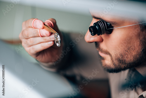 Side view of handsome watchmaker in eyeglass loupe looking at wristwatch part