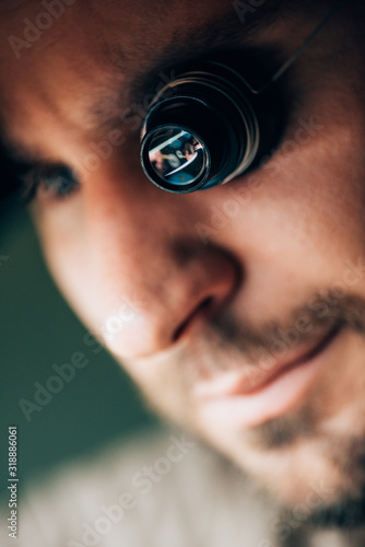 Selective focus of handsome watchmaker in eyeglass loupe looking away