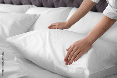 Woman fluffing soft pillow in bedroom, closeup