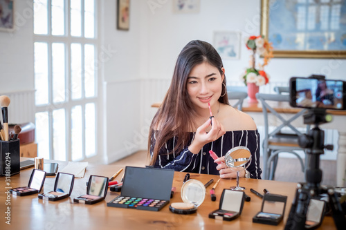 Young asian woman blogger with makeup cosmetics recording video clip online by smartphone at home.