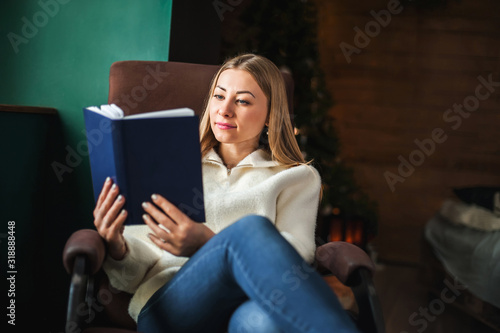 young woman sits in a comfortable chair in a white warm sweater and reads a book © algae5