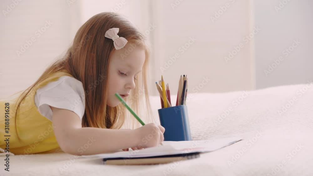 Side view of cute child drawing with pencils and paper on bed Side view of cute child drawing with pencils and paper on bed