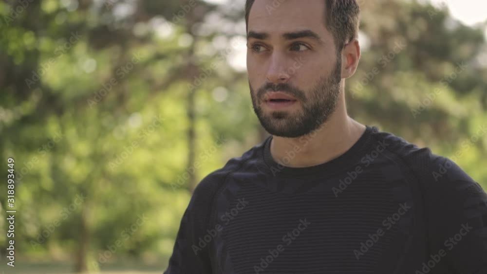 Pensive handsome sportsman thinking about something and looking around while using smartphone in park outdoors Pensive handsome sportsman thinking about something and looking around while using smartphone in park outdoors