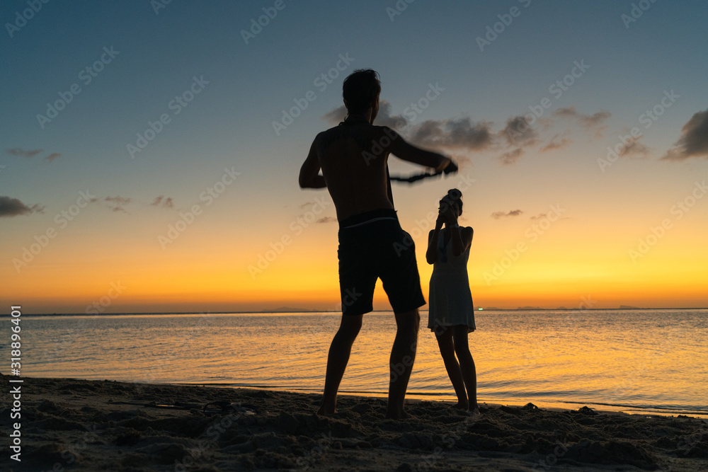 Silhouettes of a young couple on the beach on a summer sunset background  