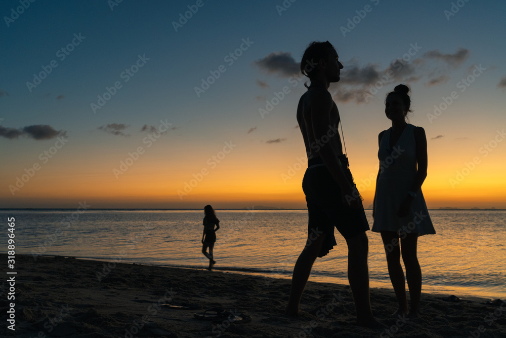 Silhouettes of a happy young couple on the beach on a summer sunset background  
