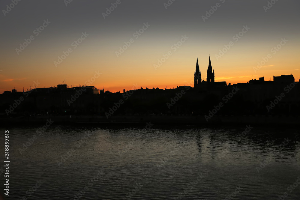 Silhouette of the skyline of the city of Bordeaux, at sunset with church steeples & the river Garonne in the foreground, France.