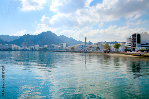 Waterfront of the city of Muscat, Oman, with buildings in the foreground & surrounded by mountains behind.