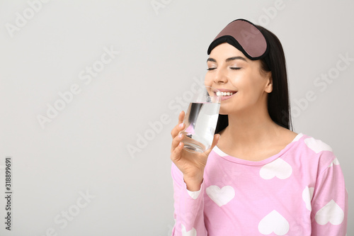 Beautiful young woman with glass of water on light background