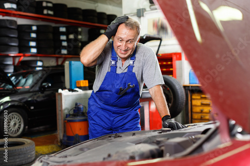 Puzzled male mechanic inspecting broken car and determining scope of work at auto service © JackF