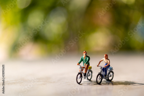 Miniature people  ride a  bicycle outdoors with green bokeh background