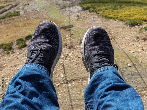 Men's legs in blue jeans and sneakers above the ground